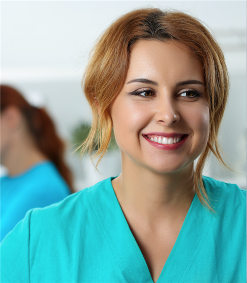 Nurse in green smock smiling to someone off camera. 